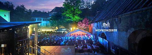 Abendliche Außenaufnahme eines beleuchteten Konzertpublikums bei den Hofkonzerten im Schloss Syburg.